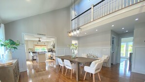 A spacious kitchen with white cabinetry, a wooden dining table, and a view to the outdoor patio. - 5BR, Luxury Home, Pool, Large Yard , Close to Beach & Town (Southampton)