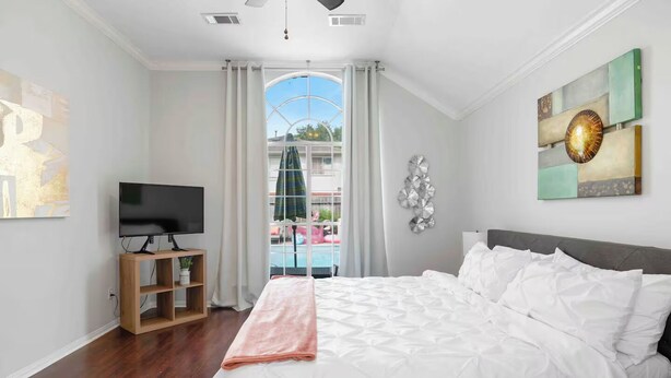 Camera da letto con un ampio letto, una TV su un mobile in legno e vista sulla piscina attraverso una porta in vetro.