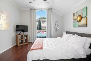 A bedroom with a large bed, a TV on a wooden stand, and a view of a pool through a glass door.