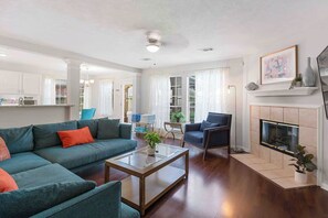 A living room with a sofa, armchair, and coffee table. There is a fireplace and a television on the wall.