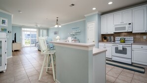 A kitchen with white cabinets, a central island, and a dining area with chairs. - Sunset Island Condo, Indoor/Outdoor Pools, FREE Linen/Towel Pkg, Parking for 2 (Ocean City)