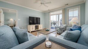 A living room with a TV, sofa, coffee table, and a ceiling fan. - Sunset Island Condo, Indoor/Outdoor Pools, FREE Linen/Towel Pkg, Parking for 2 (Ocean City)