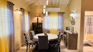A dining area with a round table, patterned chairs, a central lamp, and a small cabinet with decorative items. - Tropical Getaway Home (Frederiksted)