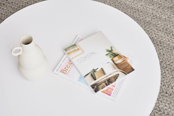 A white round table with a white ceramic pitcher and a magazine titled "COASTAL" featuring home decor.