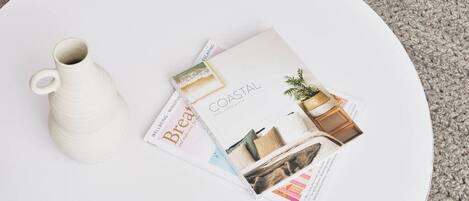 A white round table with a white ceramic pitcher and a magazine titled "COASTAL" featuring home decor.