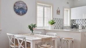 Une cuisine moderne avec des meubles blancs, une grande horloge et un coin repas comprenant des chaises et une table, le tout dans des tons blancs.