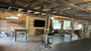 A rustic interior with wooden beams, a bar area, seating, and a TV mounted on the wall.