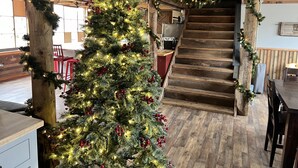 A Christmas tree decorated with lights and ornaments in a rustic interior with wooden beams and a staircase.
