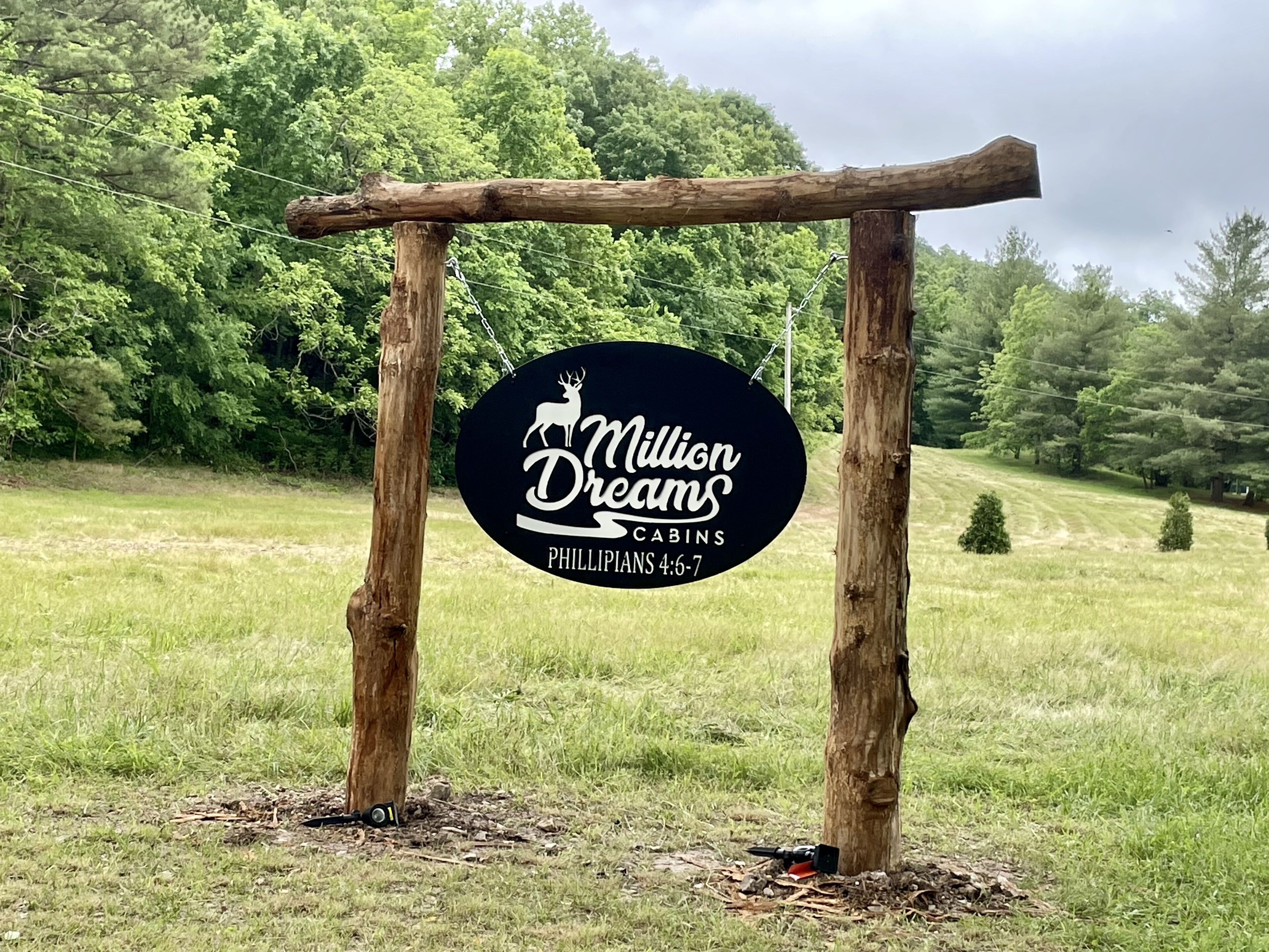 Un senyal de fusta amb un logotip i text que indica 'Million Dreams Cabins' a Filipenses 4:6-7.