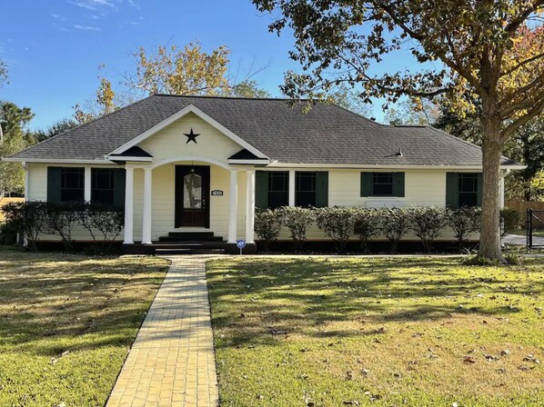 A single-story house with a dark roof, a front porch with white columns, and a star-shaped window above the door.