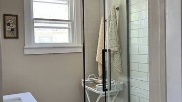Une salle de bain avec une douche à parois de verre, un lavabo blanc, une fenêtre et un porte-serviettes.