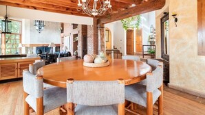 Uma mesa de jantar de madeira com cadeiras, um candelabro e uma parede de tijolos.