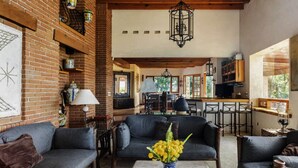 Uma sala de estar acolhedora com lareira, assentos confortáveis e uma cozinha visível ao fundo.
