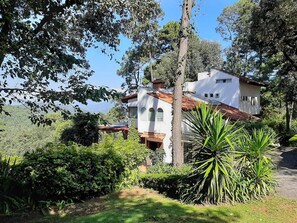 A white villa with a red-tiled roof, surrounded by lush greenery and trees.