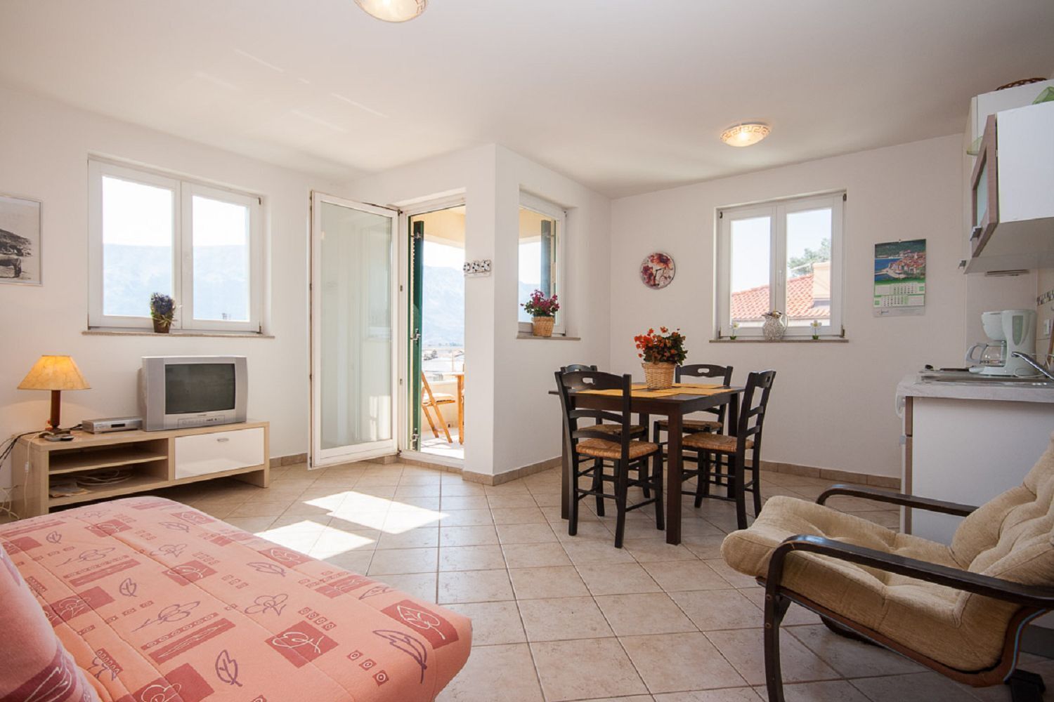 A compact living space with a bed, a dining area, a TV, and a kitchenette.