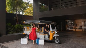 A tuk-tuk parked in front of a building with a woman in a red dress standing beside it. - Oakwood Studios Sukhumvit Bangkok (Bangkok)
