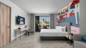 Una habitación de hotel moderna con cama, escritorio, sillón, sofá, televisor y vista a la ciudad.