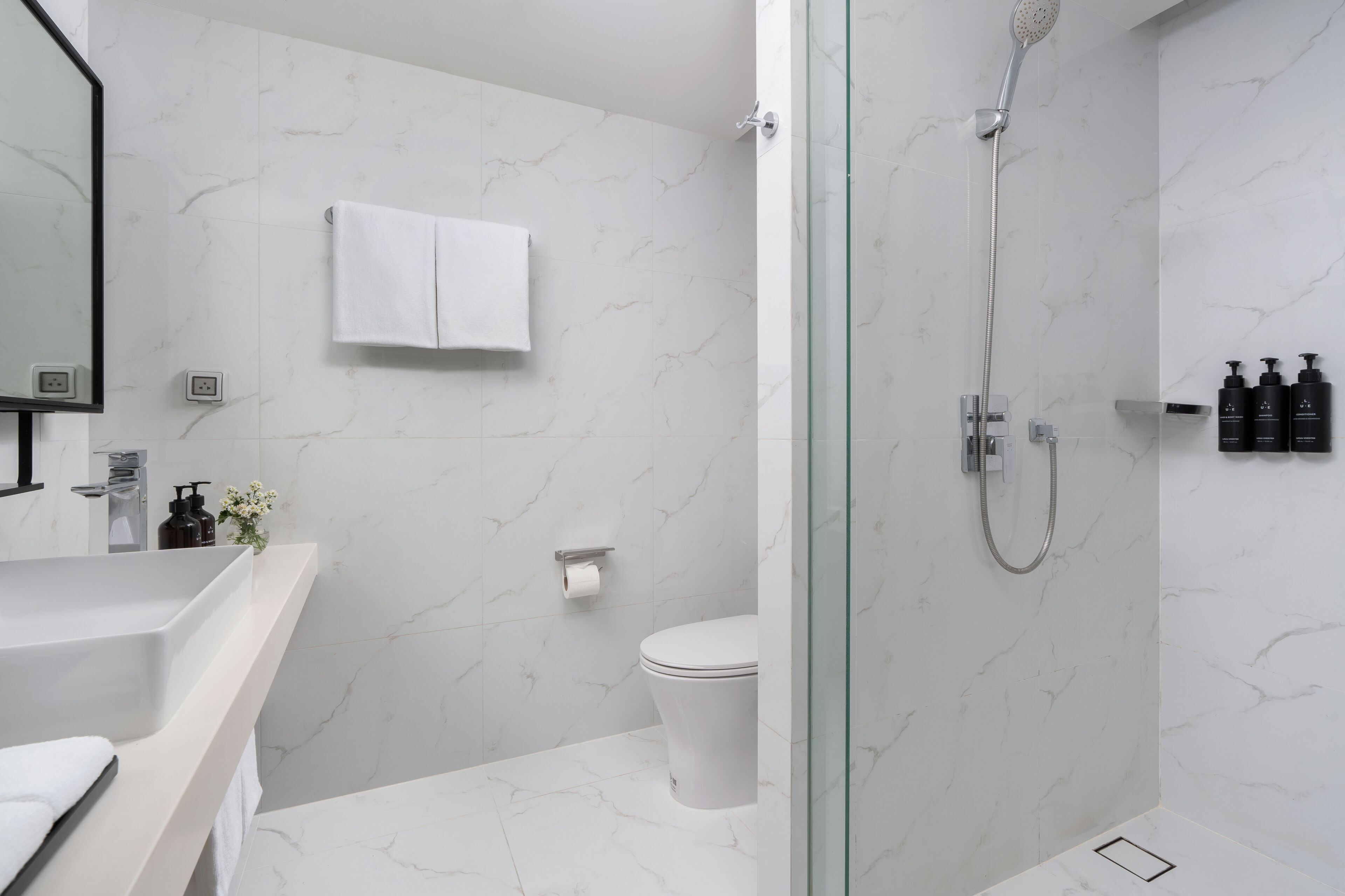Une salle de bain moderne avec une douche à parois de verre, des toilettes blanches et un mur recouvert de carreaux de marbre.