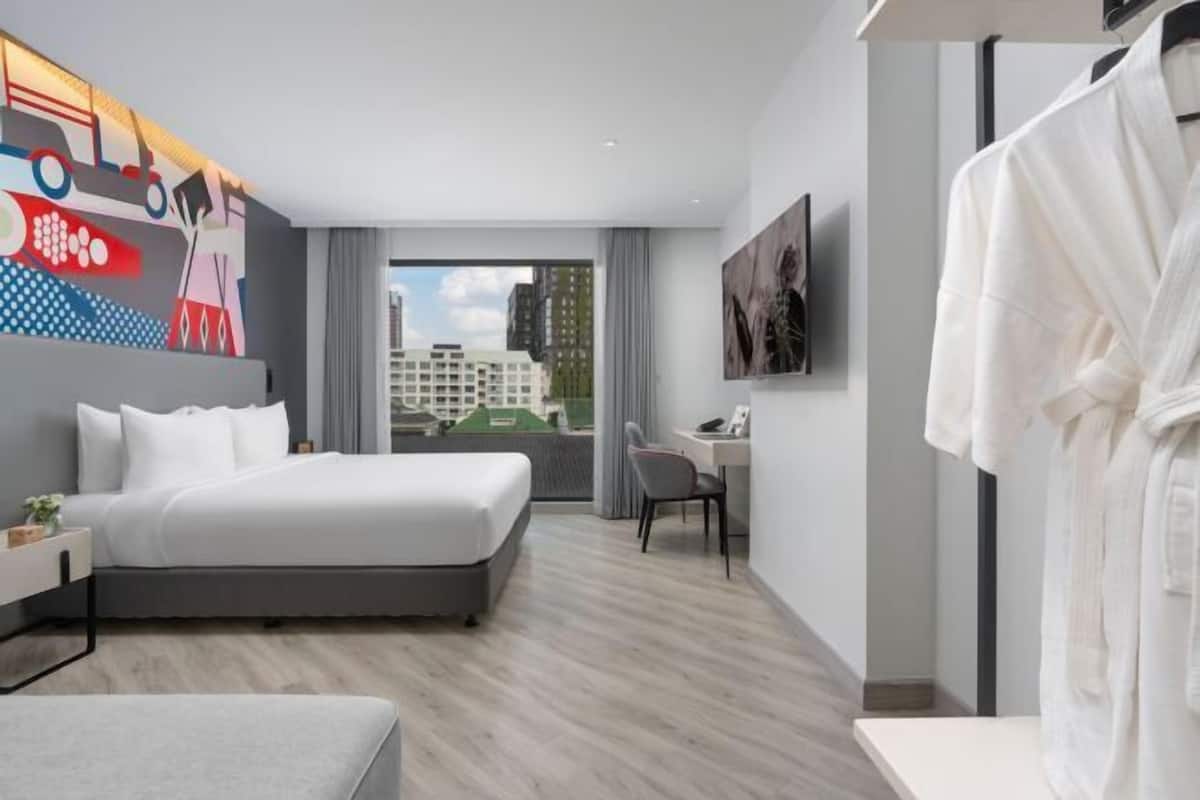 A modern hotel room with a large bed, a desk, and a view of the city.
