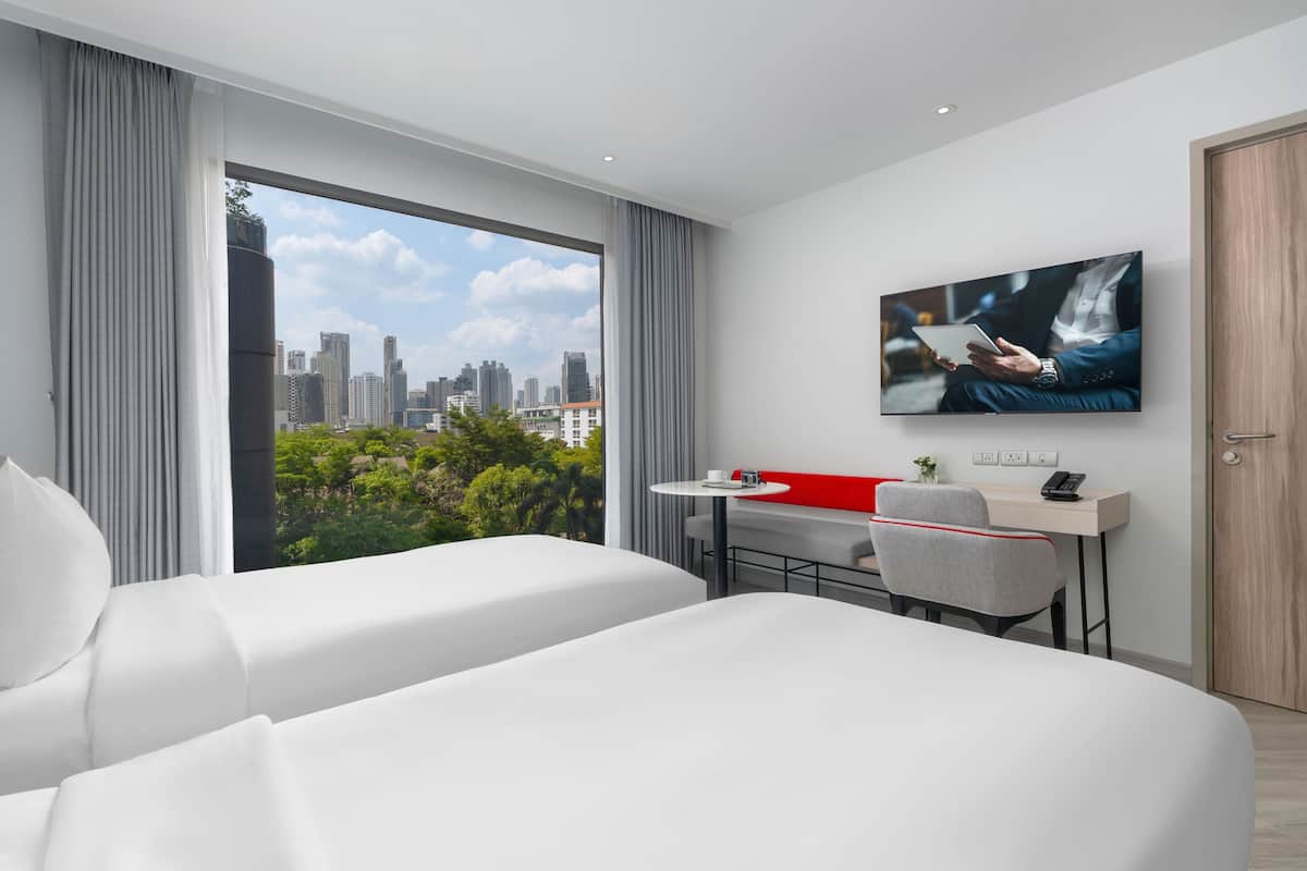 A modern hotel room with a city view, a desk with a chair, and a bed.