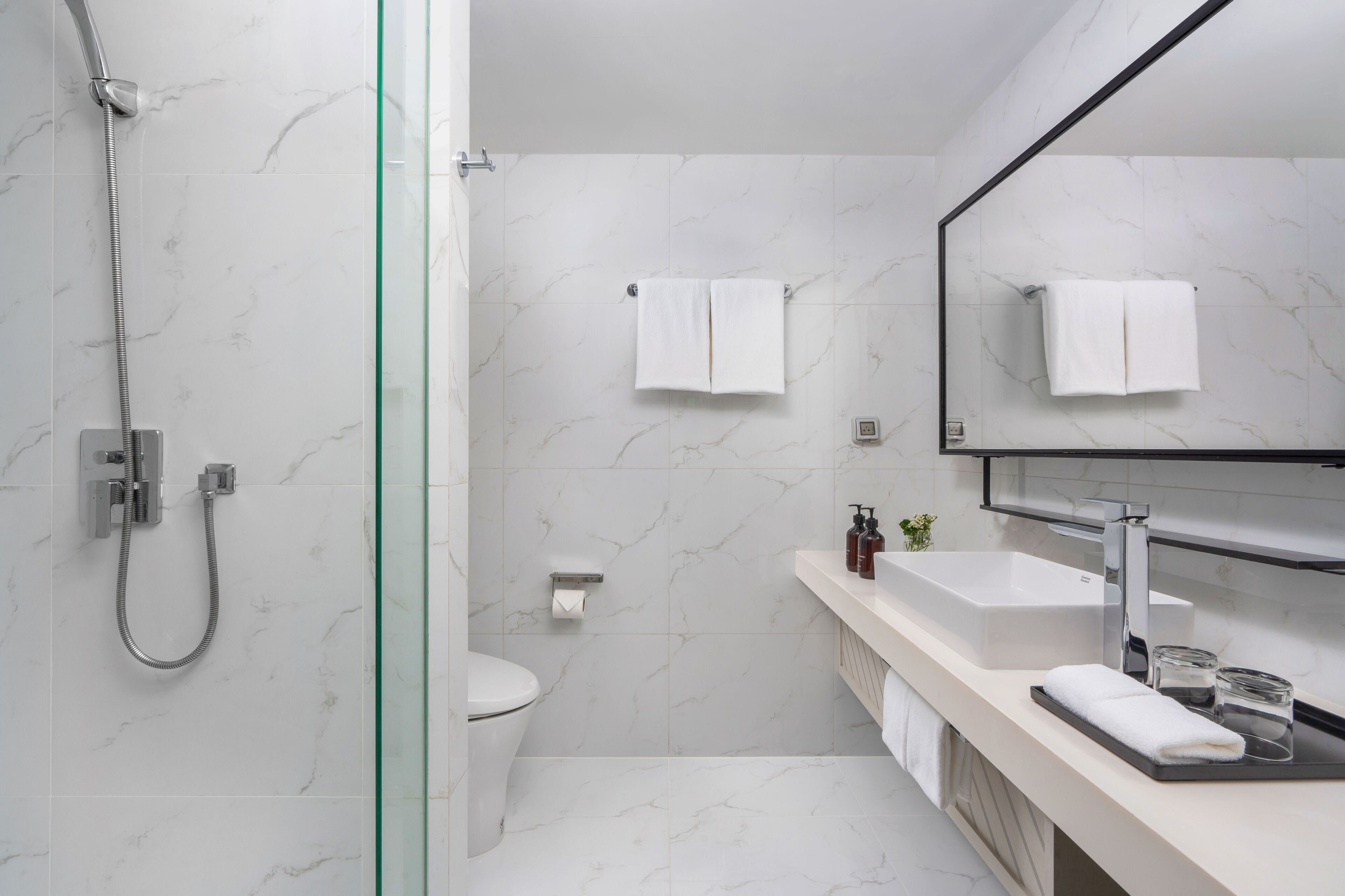 A modern bathroom with a glass-enclosed shower, a white toilet, a sink with a mirror, and a towel rack.