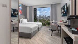 A modern hotel room with a city view, a desk with a laptop, a bed, and a seating area with a chair. - Oakwood Studios Sukhumvit Bangkok (Bangkok)