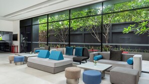 A modern outdoor seating area with sofas and ottomans, large windows with greenery outside, and a flat-screen TV mounted on the wall. - Oakwood Studios Sukhumvit Bangkok (Bangkok)