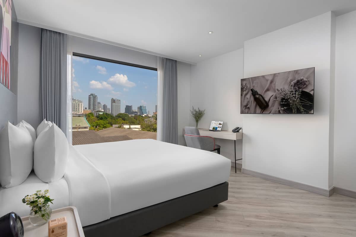 A modern hotel room with a large bed, a desk, and a city view.