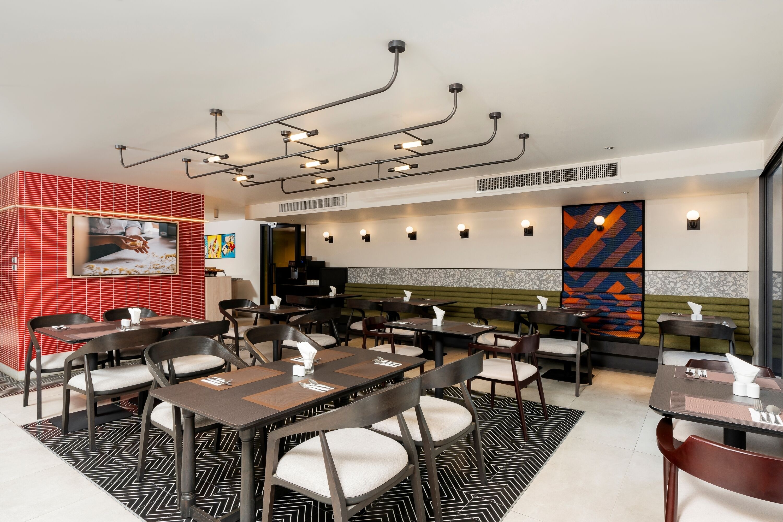 A restaurant with multiple tables and chairs, a modern ceiling design, and a red and white tiled wall.