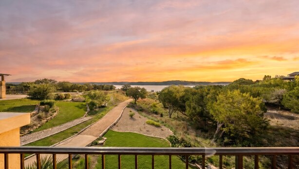 Zona ajardinada con senderos, árboles y vistas al lago al atardecer.