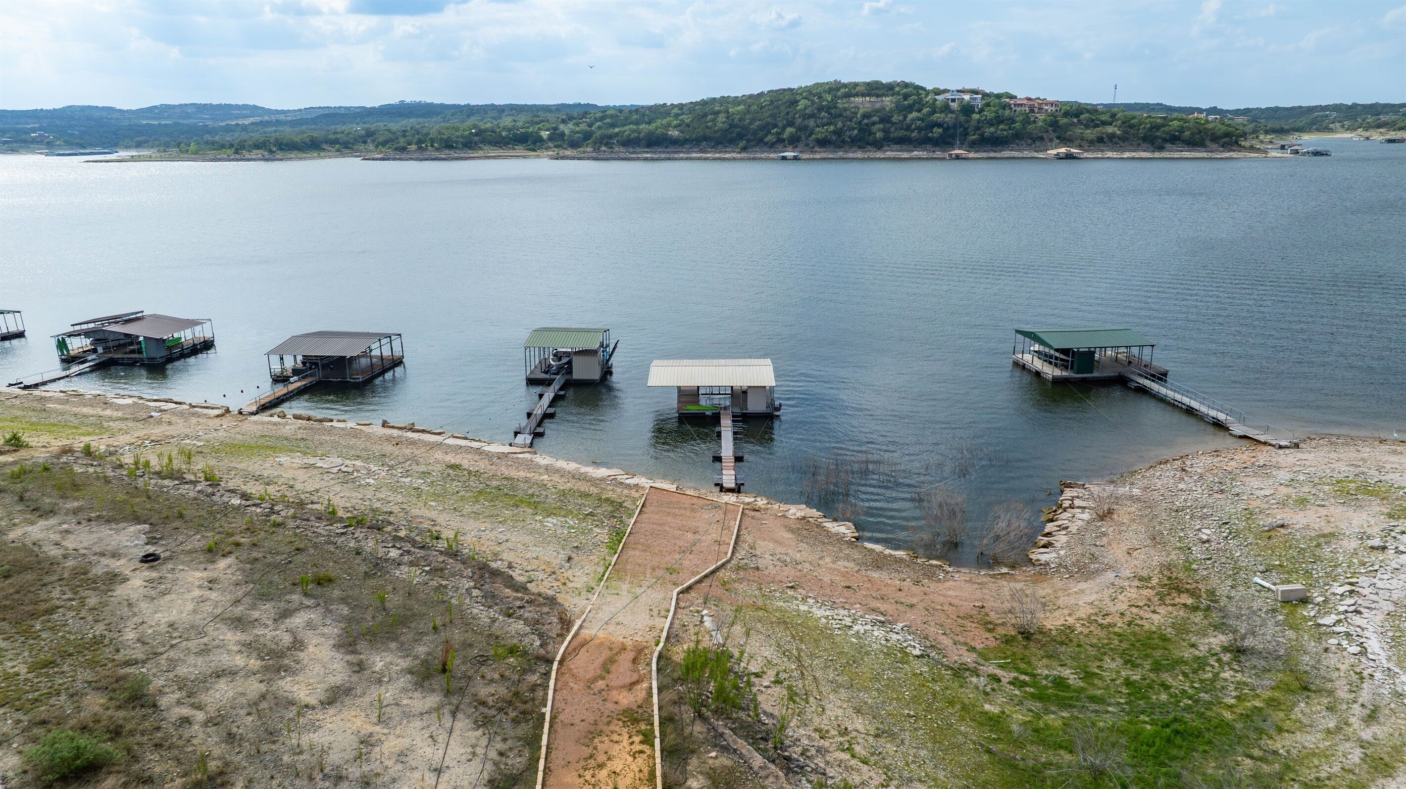 A lakeside property with multiple docked boats, a dock extending into the water, and a hilly landscape in the background.