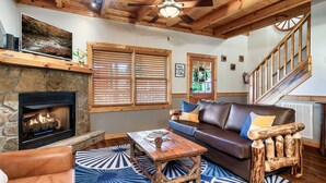 A cozy living room with a stone fireplace, wooden ceiling beams, a leather sofa, and a rustic coffee table. - LOCATION*PET FRIENDLY*NEAR ATTRACTIONS*HOT TUB (Pigeon Forge)