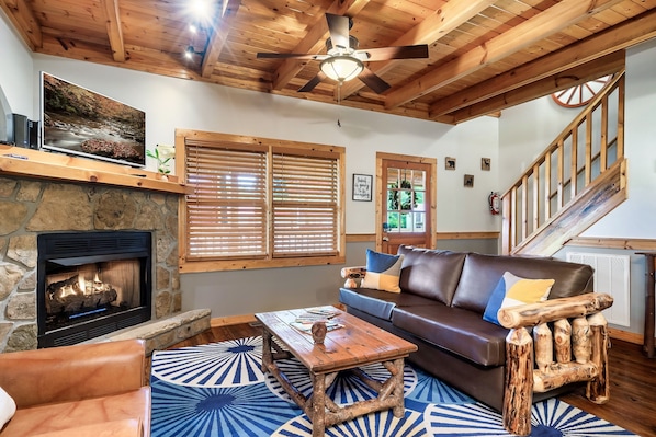 A cozy living room with a stone fireplace, wooden ceiling beams, a leather sofa, and a rustic coffee table.