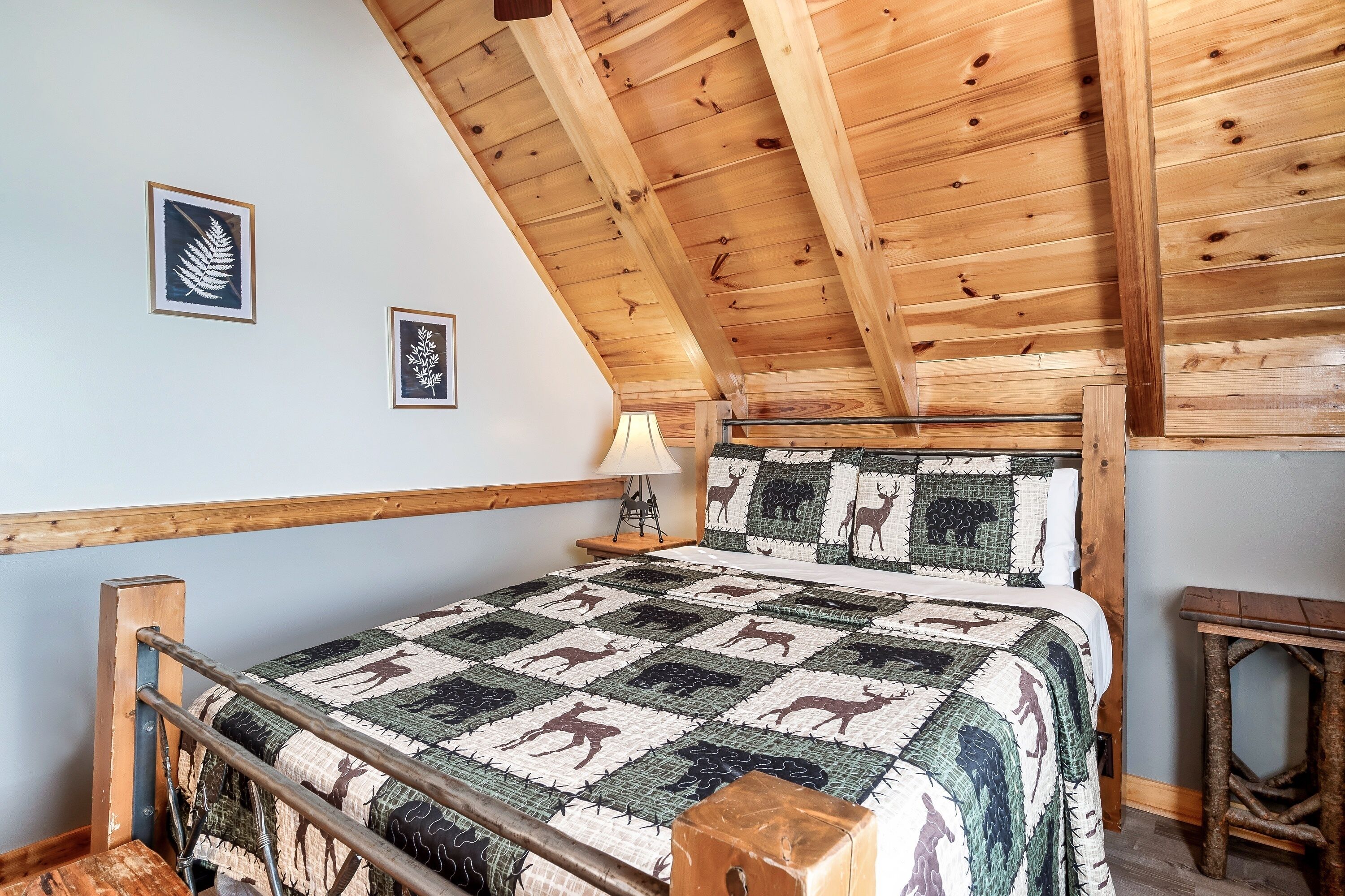 A bedroom with a wooden ceiling, a bed with a patterned quilt, a nightstand with a lamp, and a rustic bench.