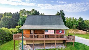 A log cabin with a porch, surrounded by greenery and trees. - LOCATION*PET FRIENDLY*NEAR ATTRACTIONS*HOT TUB (Pigeon Forge)