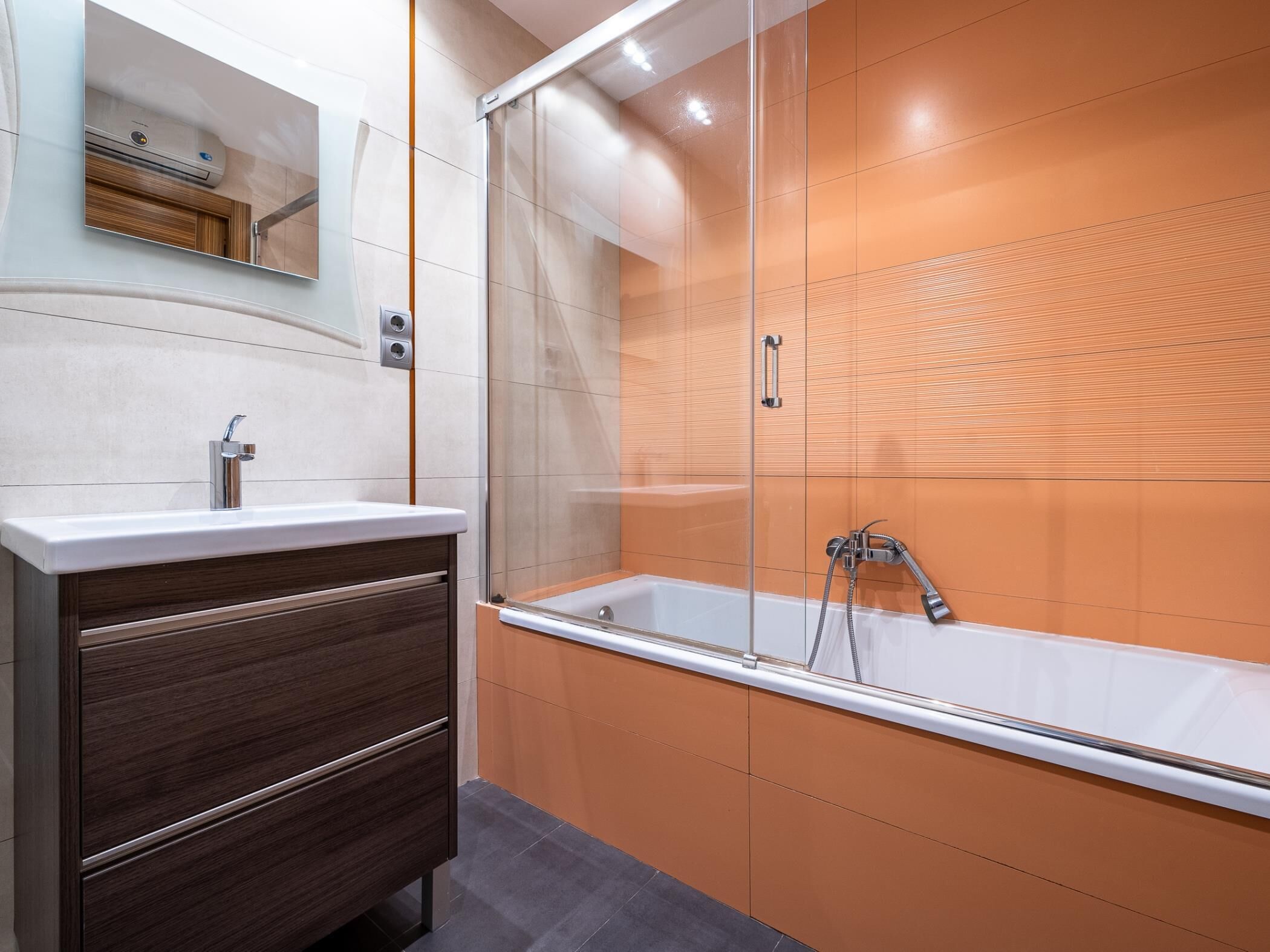 Ein modernes Badezimmer mit einer Duschkabine aus Glas, einem weißen Waschbecken und einem Holzbadschränkchen.