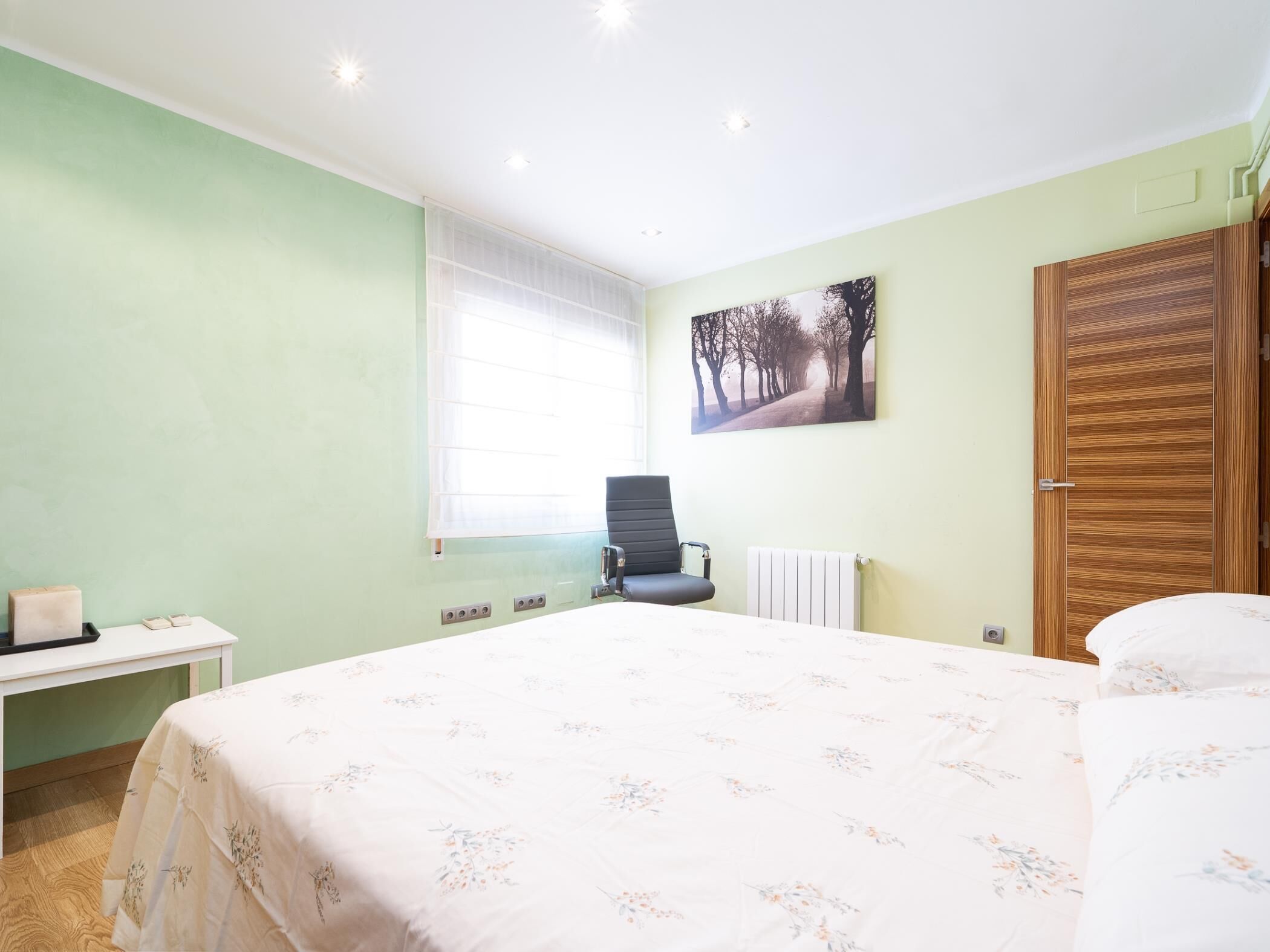 Un dormitorio con cama, una silla, una mesita de noche, un radiador y una ventana con persianas.