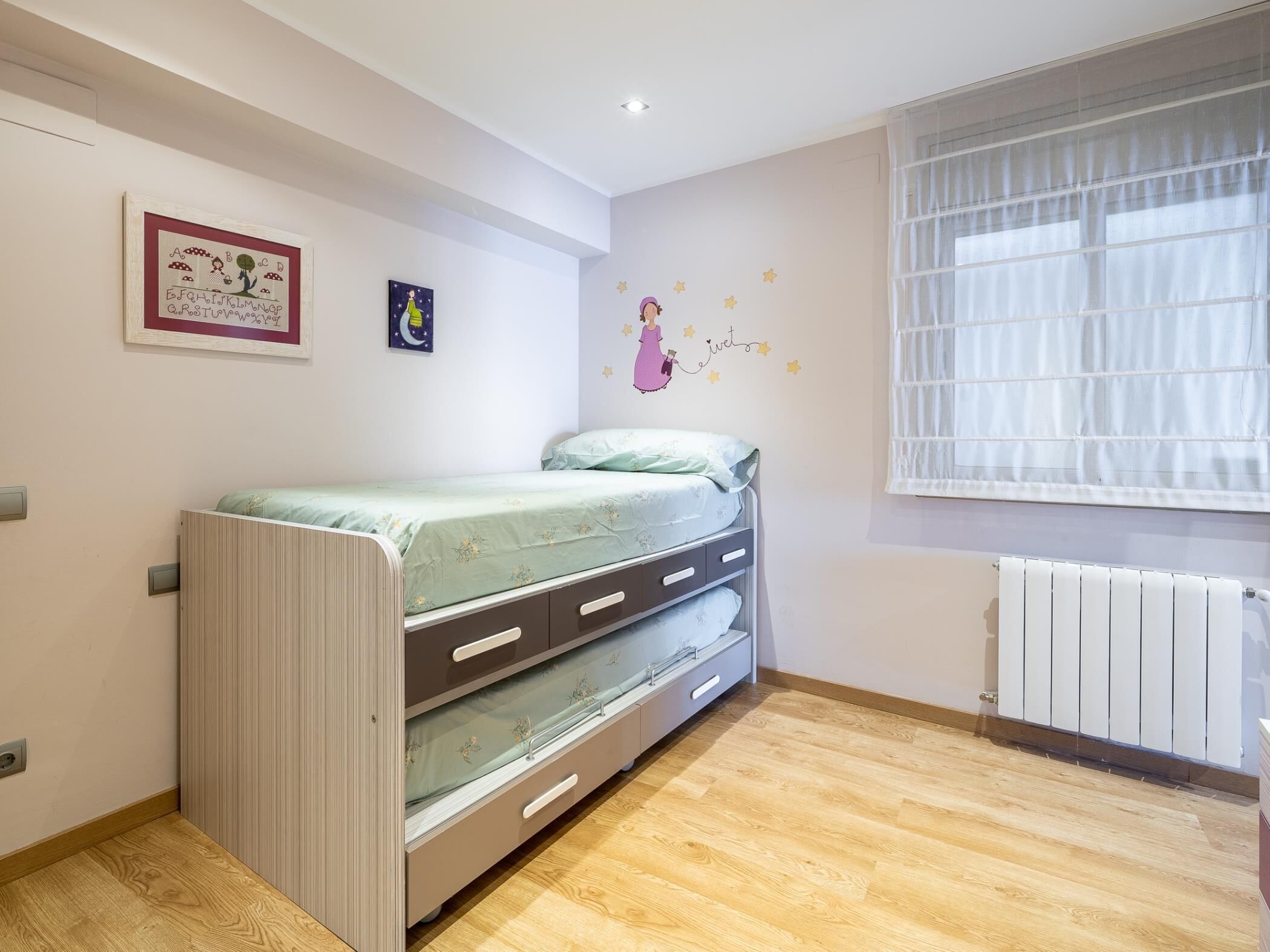 Ein Schlafzimmer mit Etagenbett, Heizkörper, einem Fenster mit Jalousien und Wanddekorationen.