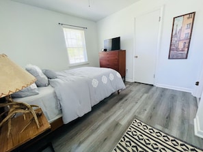 Un dormitorio con cama, cómoda, televisor y un cuadro en la pared.