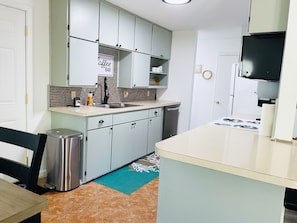 Una cocina compacta con armarios grises claros, un lavamanos de acero inoxidable y un salpicadero de azulejos.