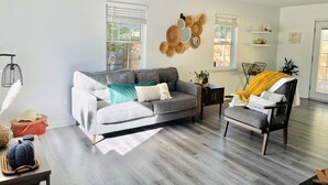 Een moderne woonkamer met een grijze bank, een houten salontafel en een gele plaid.