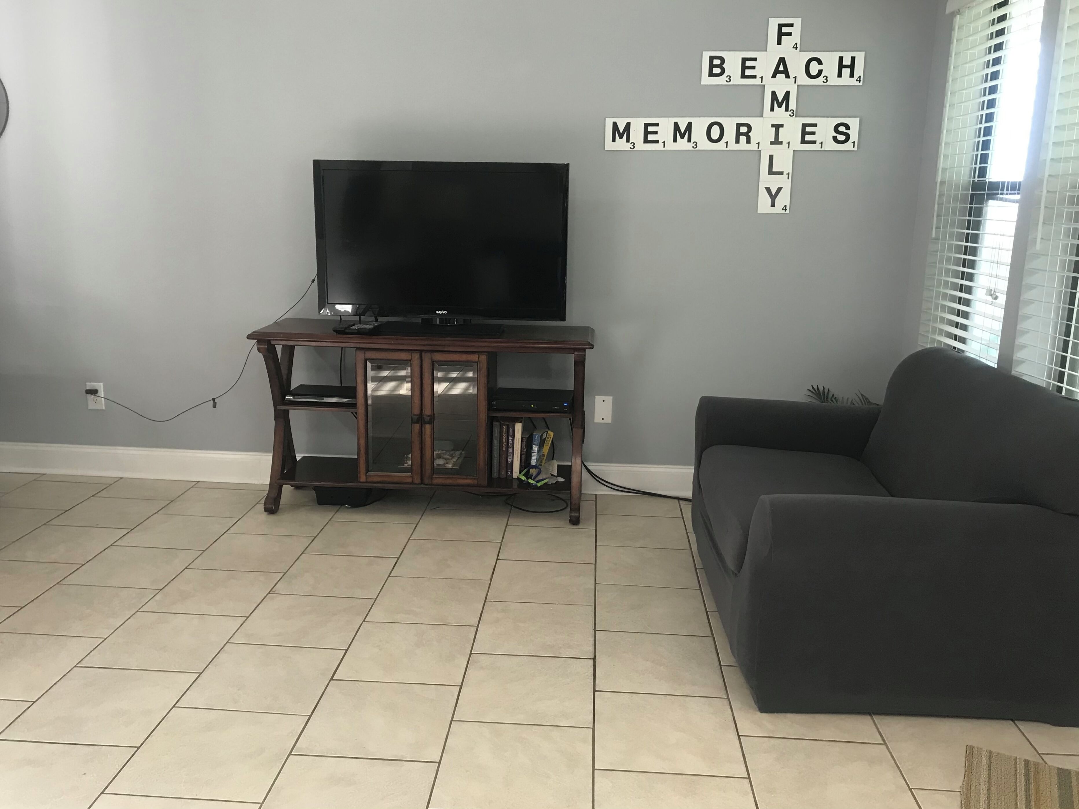 A living room with a dark sofa, a wooden entertainment unit with a flat-screen TV, and a wall-mounted crossword puzzle.