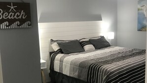 Ett sovrum med en säng, ett sängbord, en vägglampa, en takfläkt och en dekoration med strandtema.