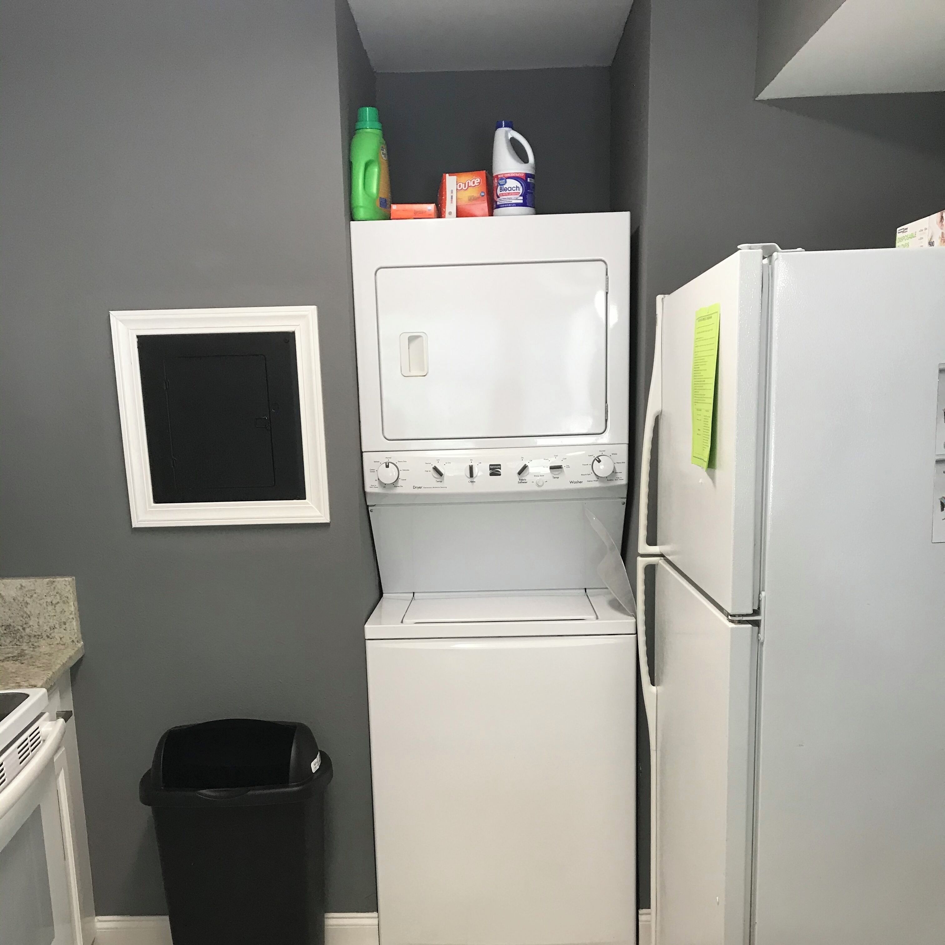 A compact laundry room with a washer and dryer, a small trash bin, and a refrigerator.
