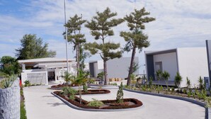 A modern building with a white exterior, surrounded by landscaped gardens and trees.