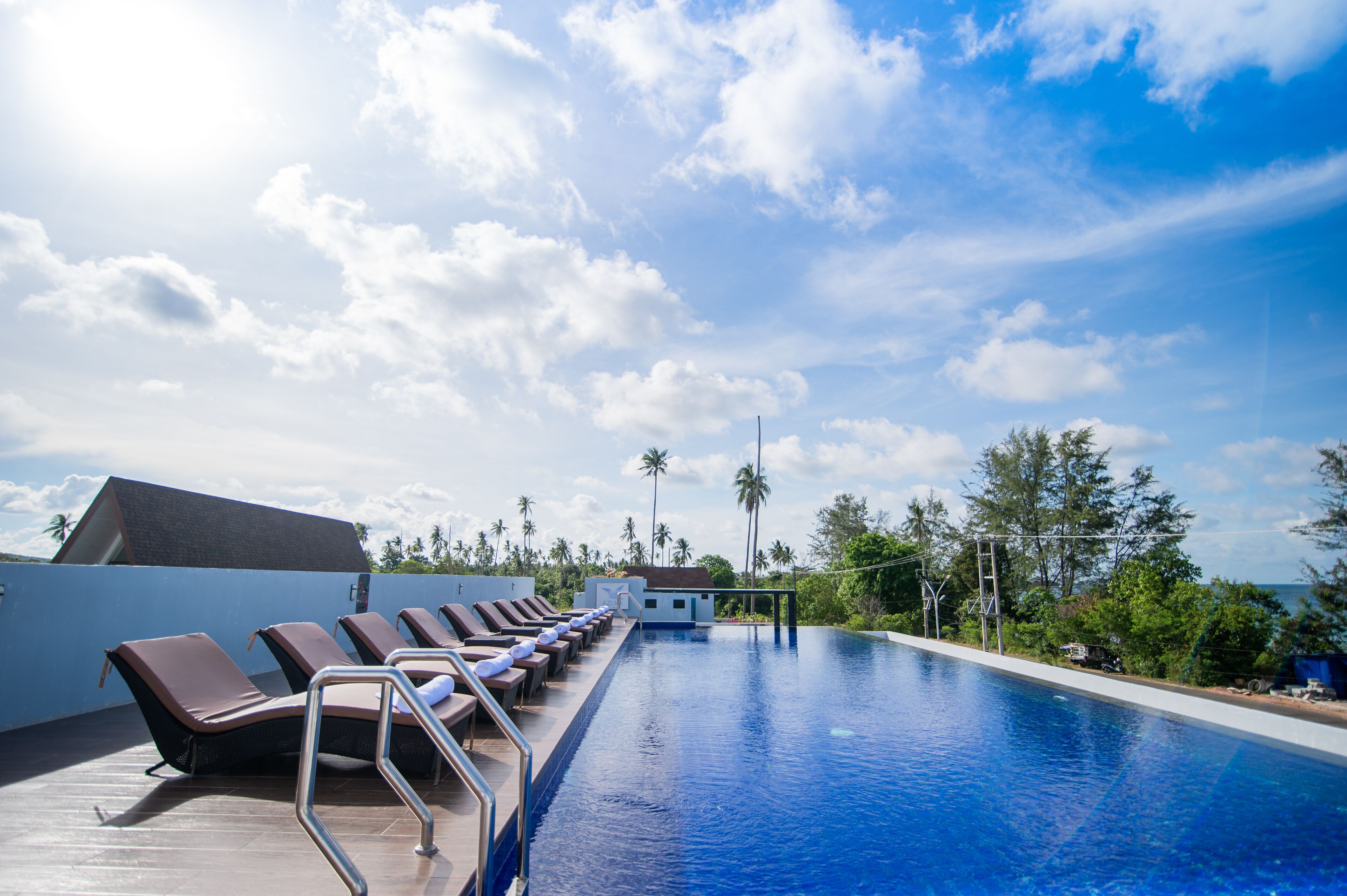 A rooftop infinity pool with lounge chairs and a view of palm trees and the ocean.