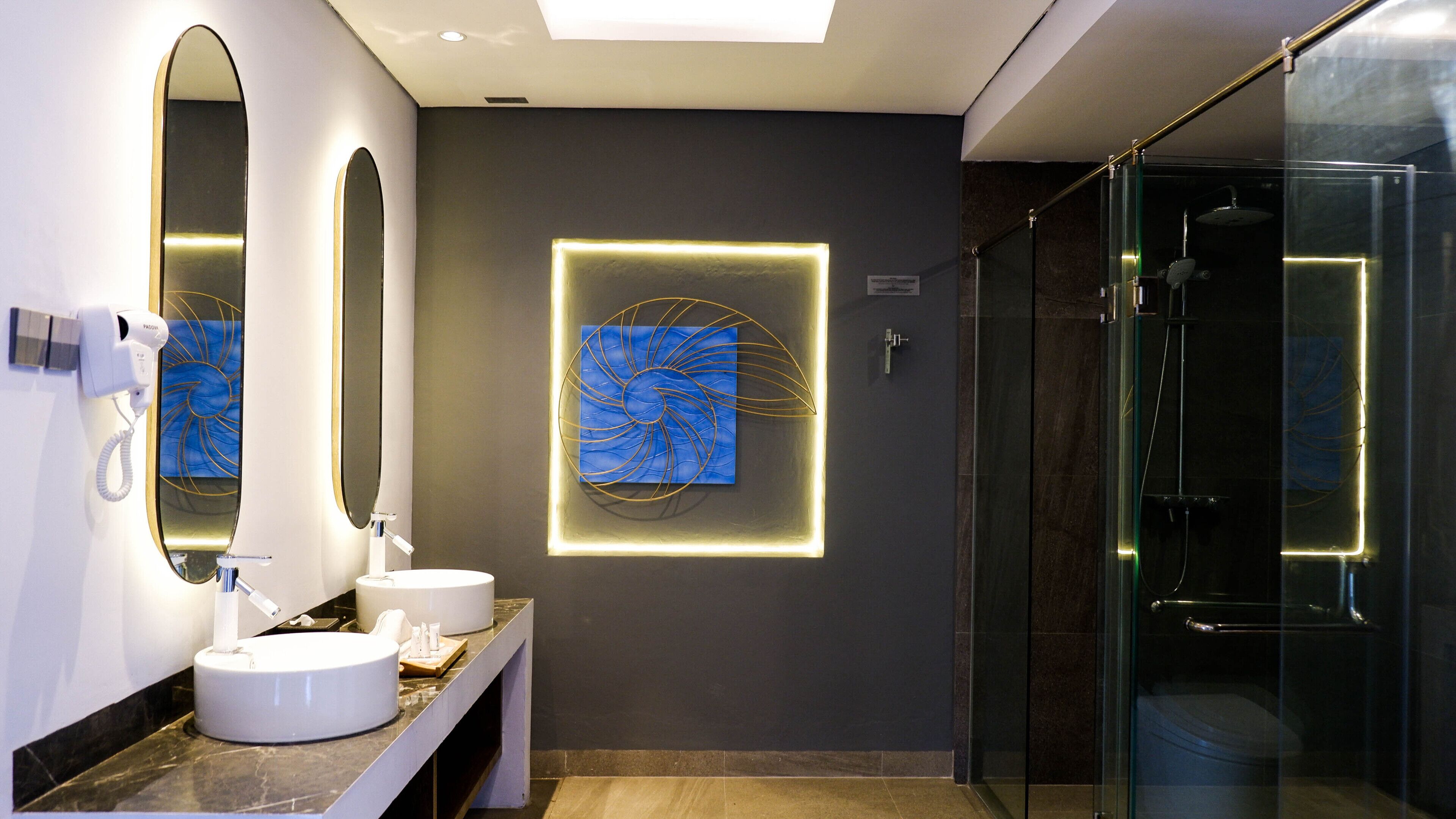 Une salle de bain moderne avec un grand miroir, deux vasques et une cabine de douche en verre.