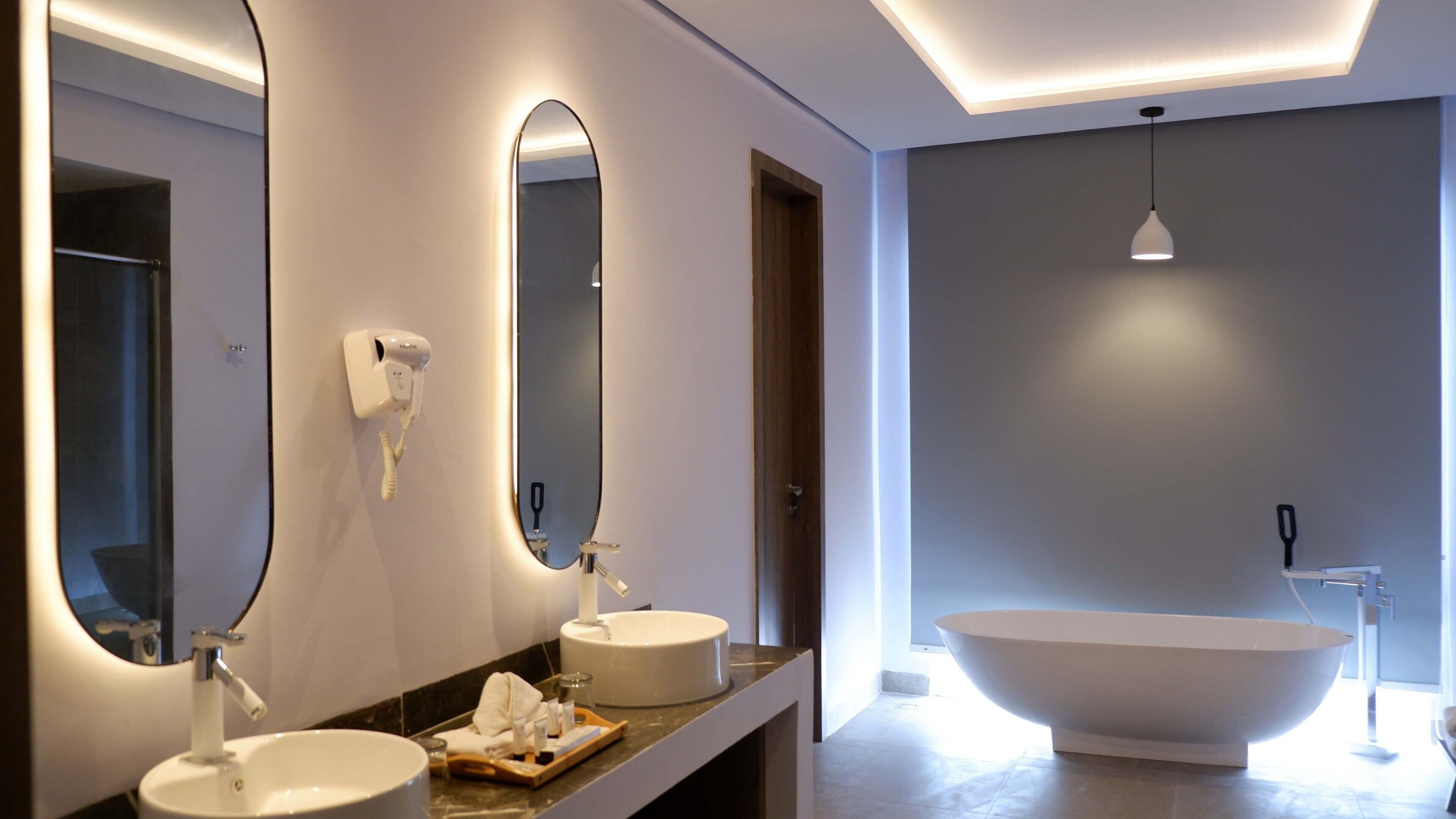 A modern bathroom with two sinks, a large freestanding bathtub, and a hairdryer mounted on the wall.