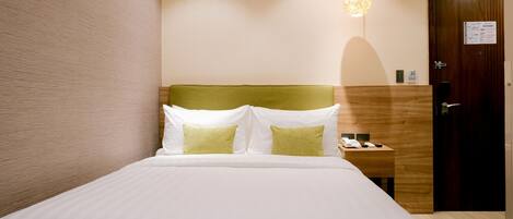 A hotel room with a bed, a nightstand, a wooden headboard, a wall-mounted light fixture, and a door with a sign.