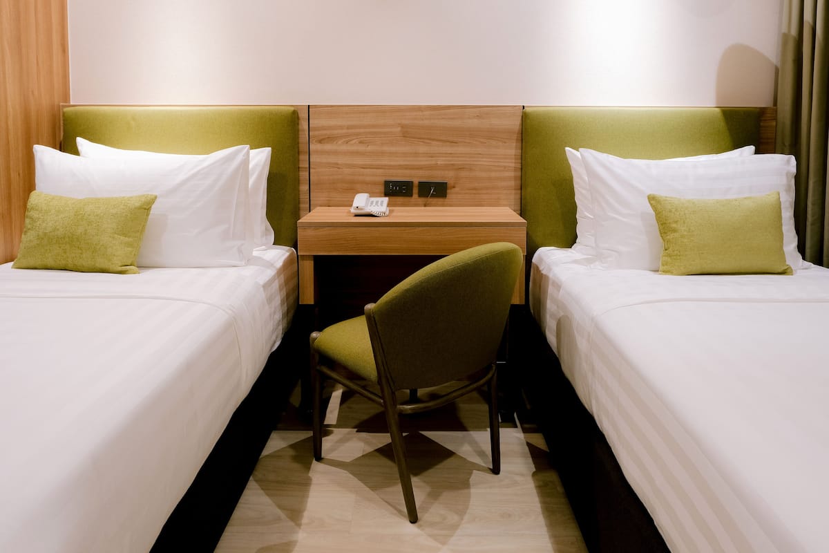 A hotel room with two single beds, a desk with a telephone, and a chair.